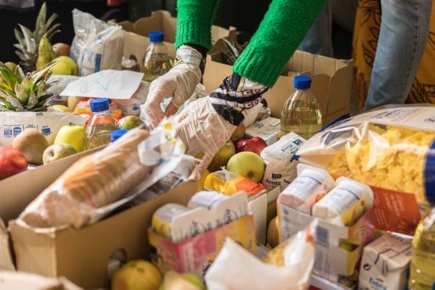 Foto donde se ven cajas con alimentos y una mano enguantada poniendo un pan en caja
